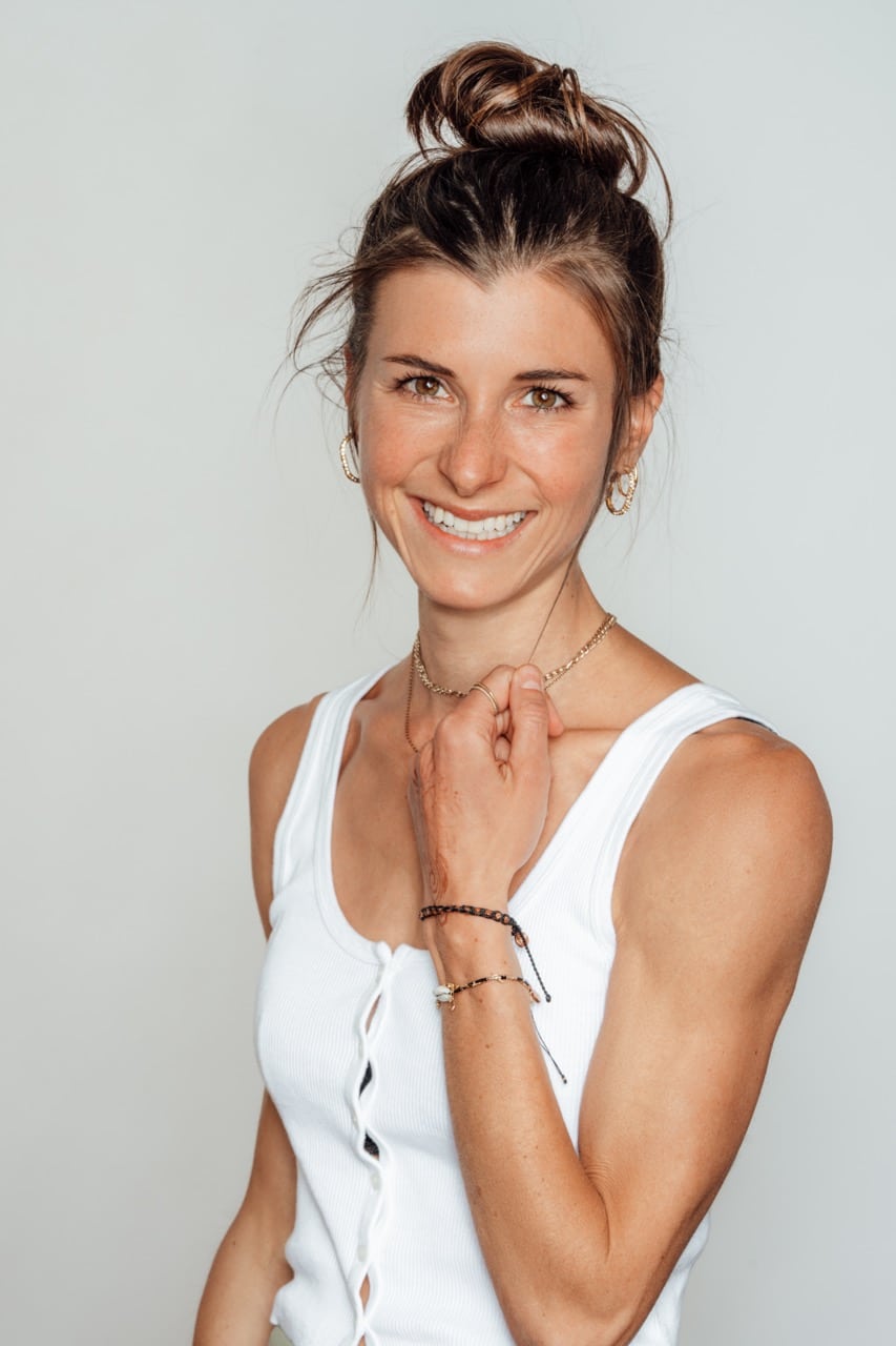 Annelina Waller steht lachend vor einer weißen Wand. Sie trägt ein weißes Top und einen Dutt.