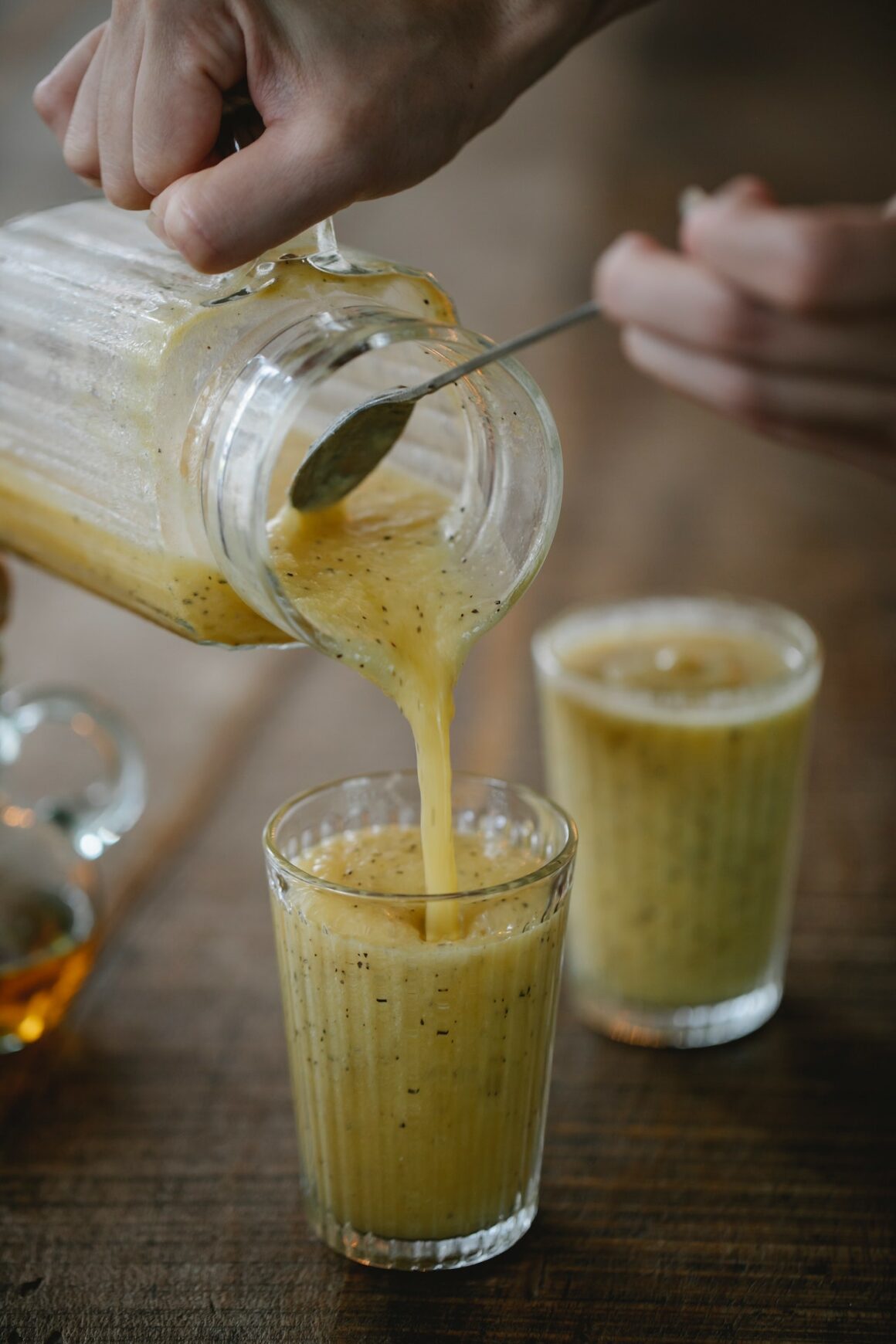 Glas Karaffee mit gelbem Smoothie welcher in ein Glas geschüttet wird