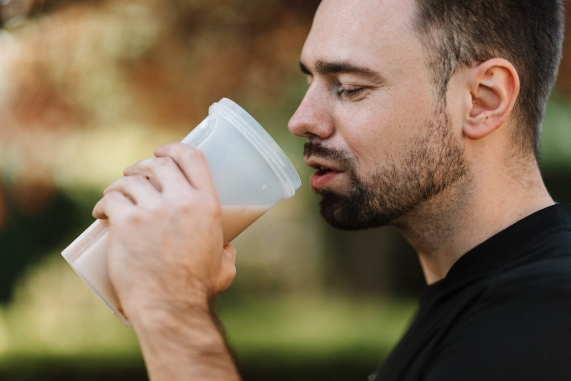 Mann hält Plastikbecher mit Proteinshake in der Hand und führt den Becher zum Mund