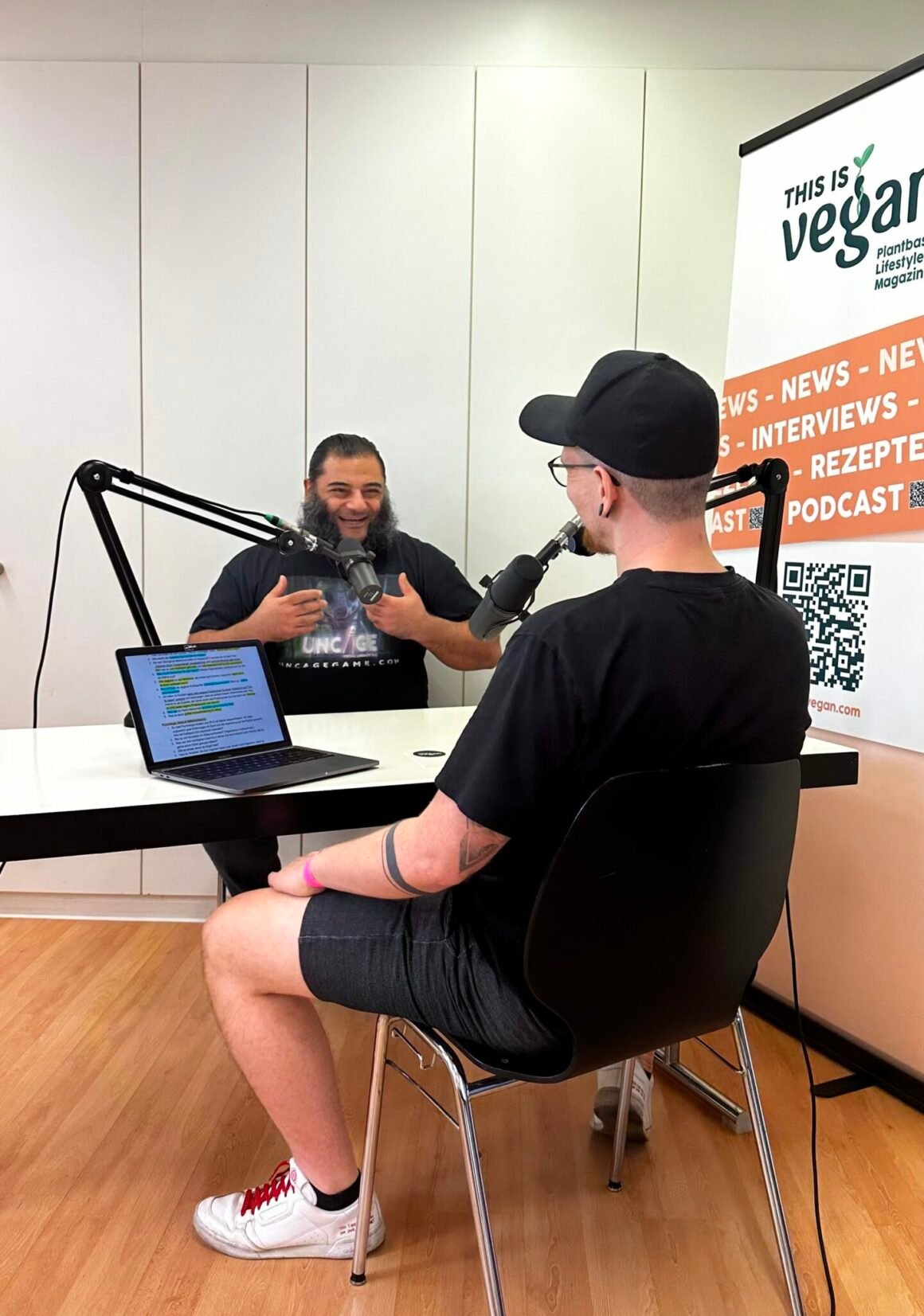 Yannick und Patrik Baboumian sitzen sich an einem Tisch gegenüber, auf dem Tisch steht und Laptop und jeder der Männer hat ein Mikrofon vor sich aufgebaut