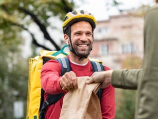 Mann mit Rucksack und Fahrradhelm übergibt eine Tüte mit bestelltem Essen