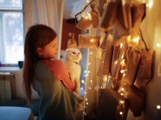 Kind mit Katze auf dem Arm steht vor ihrem veganen Adventskalender und freut sich drauf