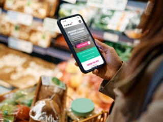 Frau probiert Veganuary 2025 aus und geht mit ihrem Smartphone und dem Veganuary-Plan im Supermarkt vegan einkaufen